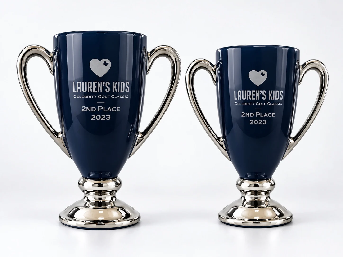 Two navy blue and silver Lauren’s Kids Celebrity Golf Classic trophy cups on a light background