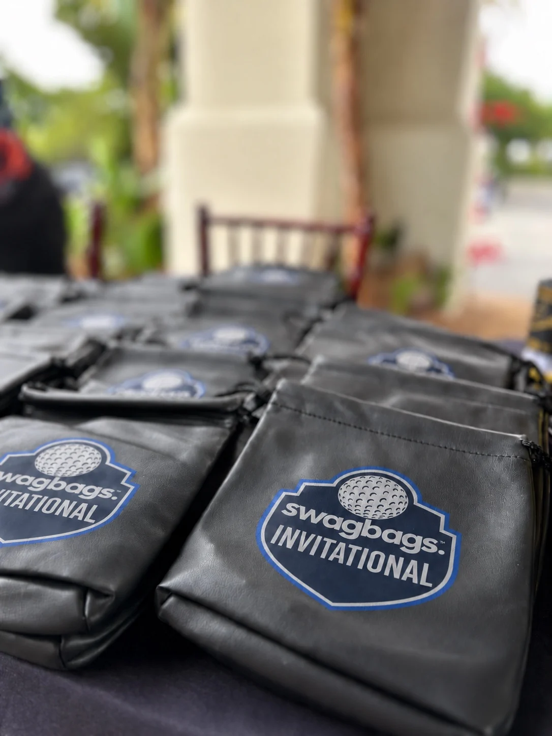Black gift pouches with blue Swag Bags Invitational crests arranged on a registration table